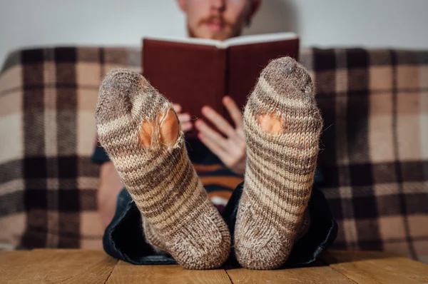 Young man reading book on couch in holey socks