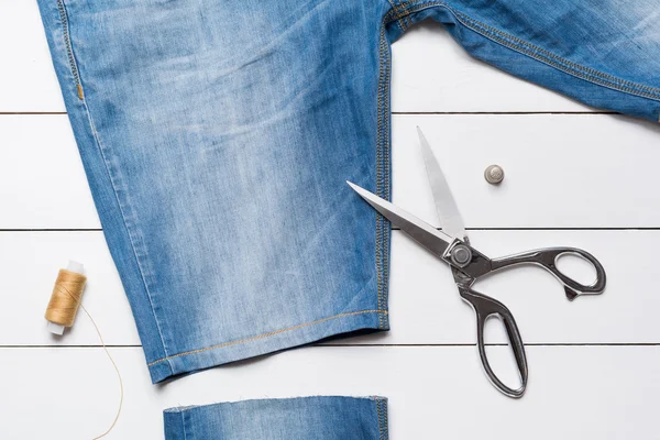 Cutting jeans with a tailor scissors to make  shorts on wooden t