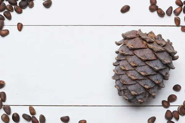 Siberian pine nuts and cone on white wooden table