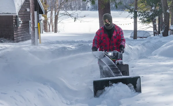 A man in work clothes, hat and gloves, operating a snow thrower / blower on a winter day in Canada.