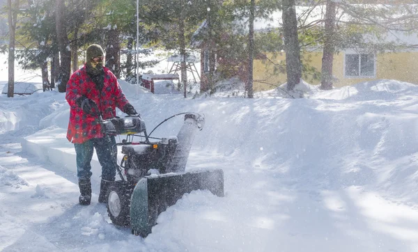 A man in work clothes, hat and gloves, operating a snow thrower / blower on a winter day in Canada.