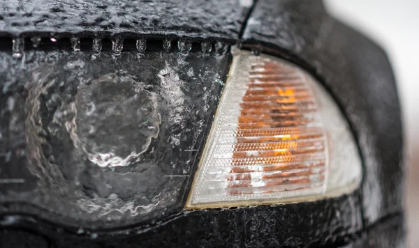 Freezing rain ice coated car.  Headlight and signal light on black car covered in freezing rain, bad driving weather in freezing rain.