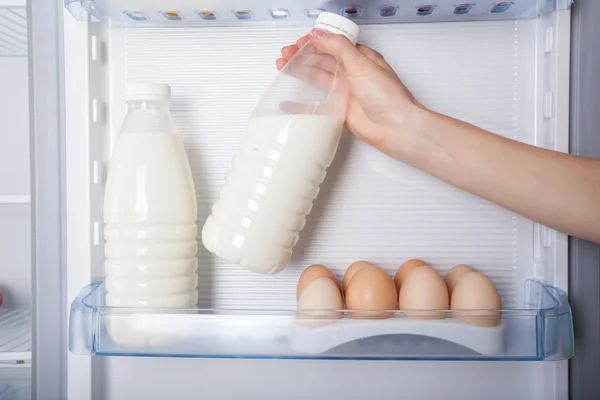 Hand reaching for bottle of milk in refrigerator