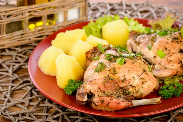 Oven baked rabbit with potatoes on red plate on wooden table.