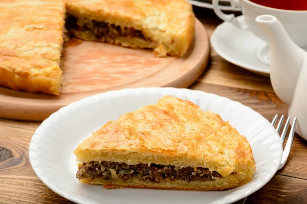 Piece of pie with minced meat on wooden table.