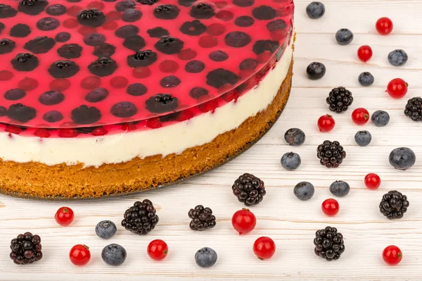 Cheesecake with jell, red currants, blueberries and blackberries on the wooden background.