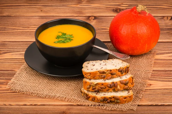 Pumpkin soup and  bread with pumpkin seeds on the wooden background.