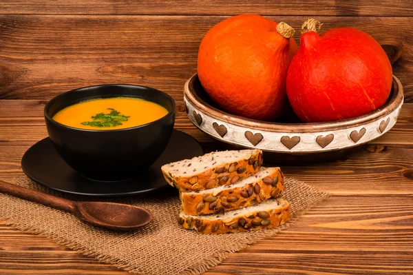 Pumpkin soup and  bread with pumpkin seeds on the wooden background.