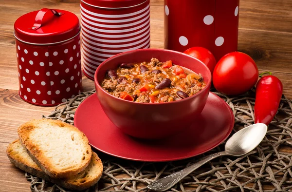 Chili con carne served in the red bowl on the wooden background.