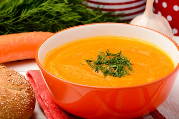 Carrot creme soup in orange bowl on the table.