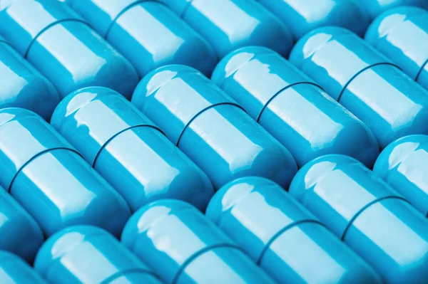 Blue softgel capsules with vitamins and minerals as background.