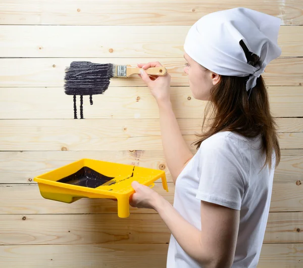 Woman painter paints the wooden wall in black