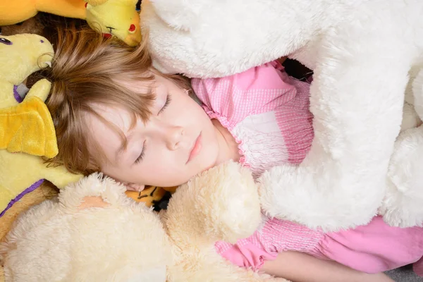 Little girl lies among stuffed toys