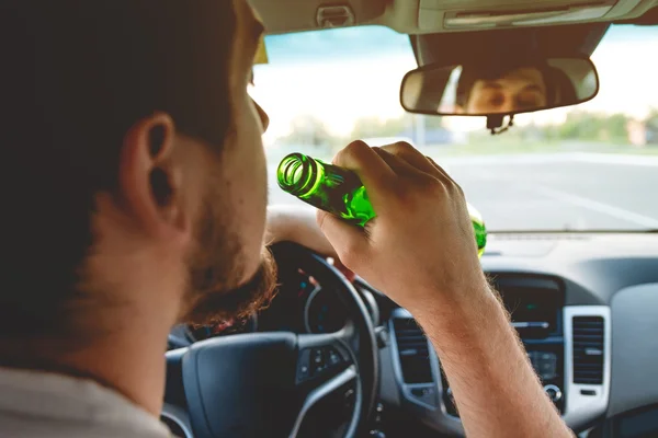 A man driving a car with a bottle of beer