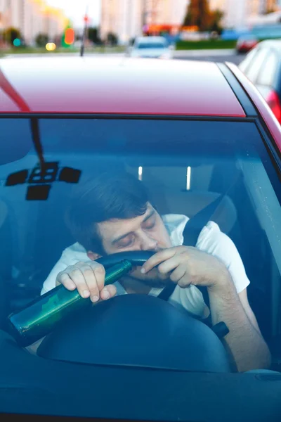 A man driving a car with a bottle of beer