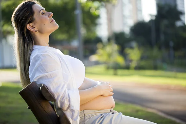 Pregnant sitting on bench in the park at sunset