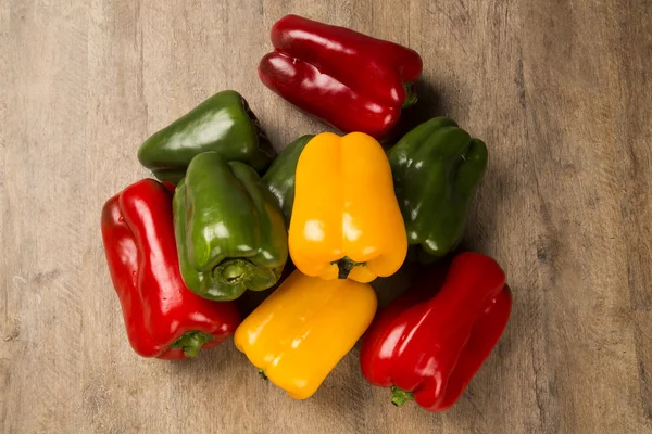 Some red, green and yellow peppers over a wooden surface