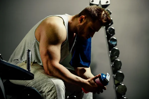 Tired bodybuilder athlete with protein shaker and towel in gym