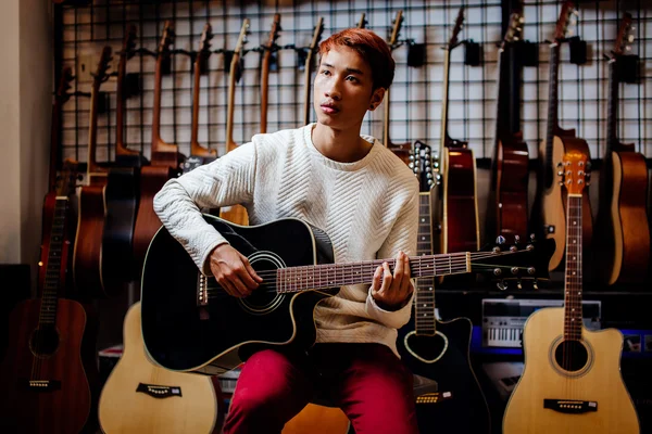 Handsome asian teenage man playing guitar in guitar shop