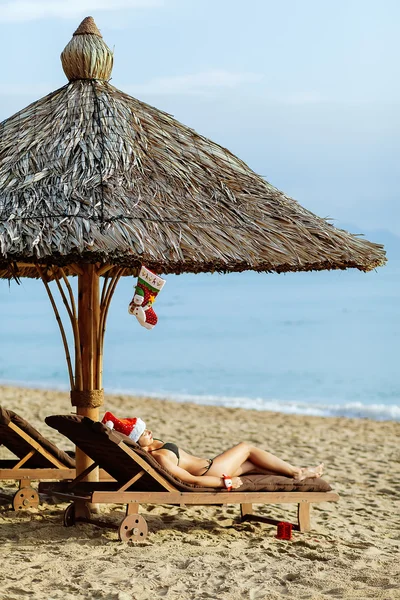 Santa girl in bikini laying on sunbed on the beach resort
