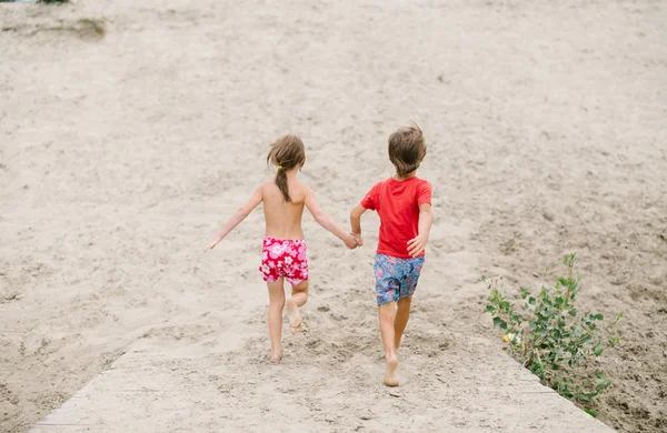 Fraternal twins run barefoot holding hands at the beach