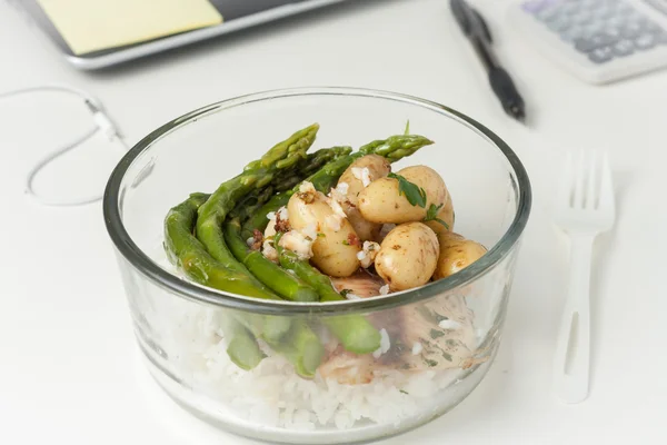 A glass container with lunch on a desk at work
