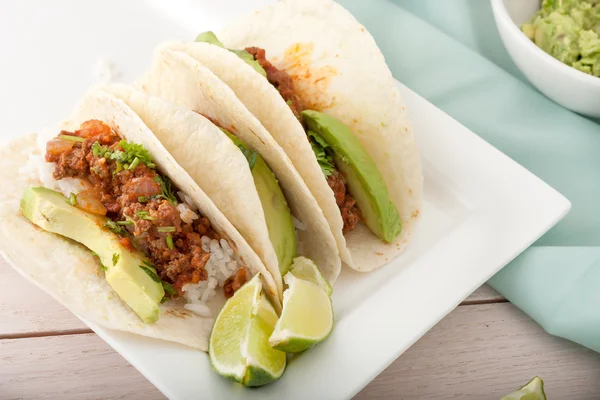 Three homemade soft tacos with ground meat, avocados, cilantro and rice