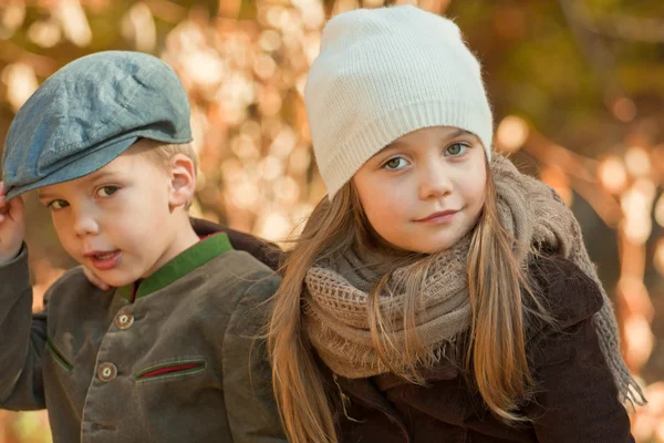 Brother and sister sitting on a bench in a park on a cool autumn day