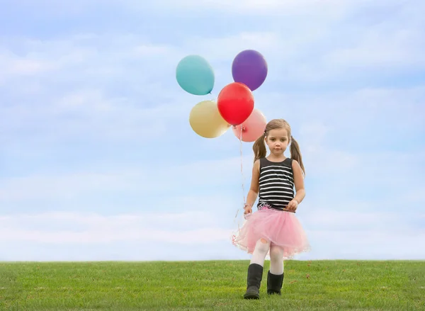 Little girl with pony tails walking down the lawn with a bunch of helium filled baloons in her hand