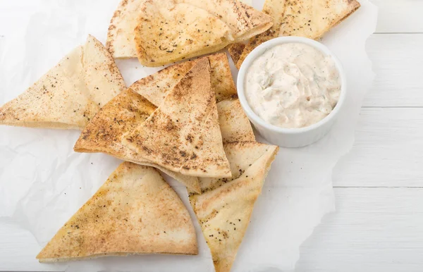 Homemade pita chips on white paper with yogurt sauce