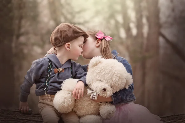 Portrait of siblings sitting together holding a teddy bear and kissing