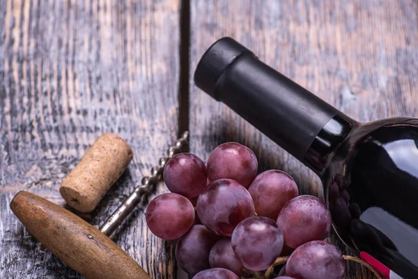 Red wine bottle, wine glass pink grapes, cheese, walnuts, corkscrew on wooden table background