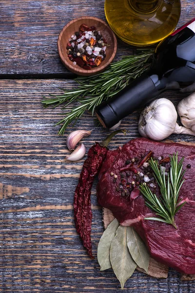 Raw beef steak with herbs and rosemary, bottle of red wine on a wooden table background