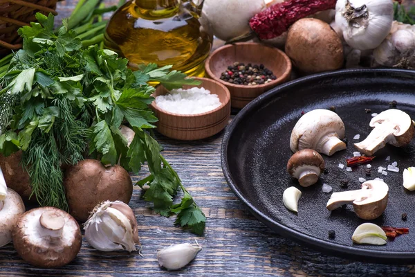 Mushrooms, parsley, dill, onion, olive oil, spices - ingredients for the preparation of mushroom dishes in a frying pan on a wooden background