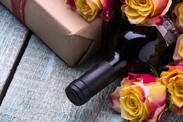 Red wine bottle, present box and flowers roses on wooden background