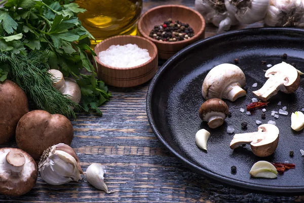 Mushrooms, parsley, dill, onion, olive oil, spices - ingredients for the preparation of mushroom dishes in a frying pan on a wooden background