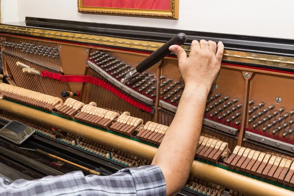 Closeup on hand tuning a upright piano using lever and tools