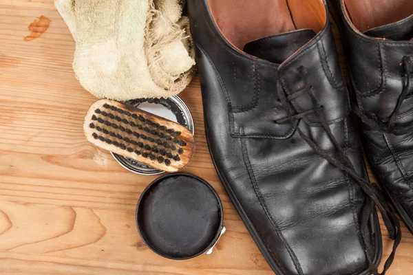 Shoe polish with brush, cloth and worn men shoes on wooden platf
