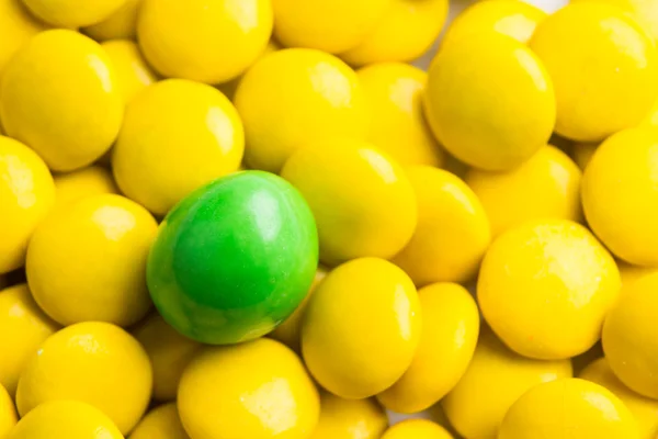 Focus on green chocolate candy against heaps of yellow candies