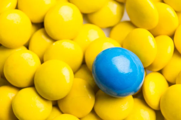 Focus on blue chocolate candy against heaps of yellow candies