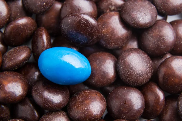 Focus on blue chocolate candy against heaps of brown candies