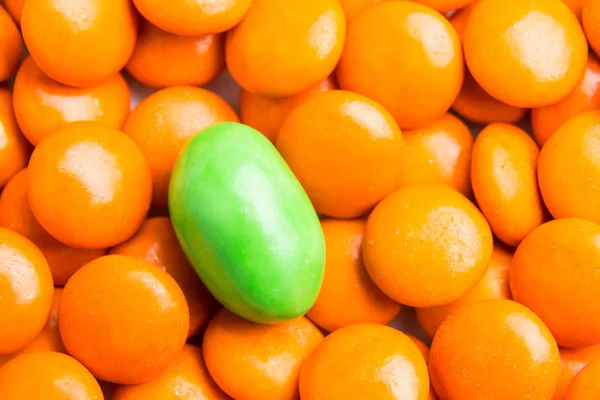 Focus on green chocolate candy against heaps of orange candies