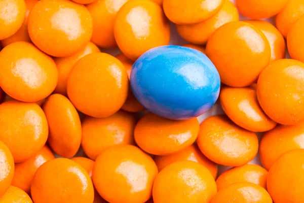 Focus on blue chocolate candy against heaps of orange candies