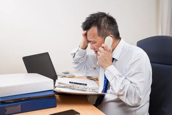Stressful and frustrated Asian manager talking on telephone in office