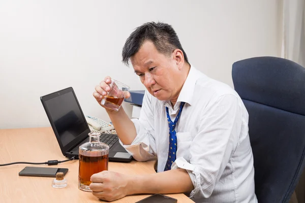 Frustrated and stressful Asian manager drinking hard liquor in office