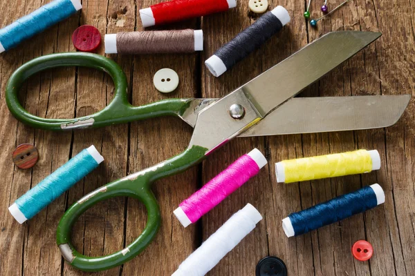 Colored thread and scissors on the wooden background