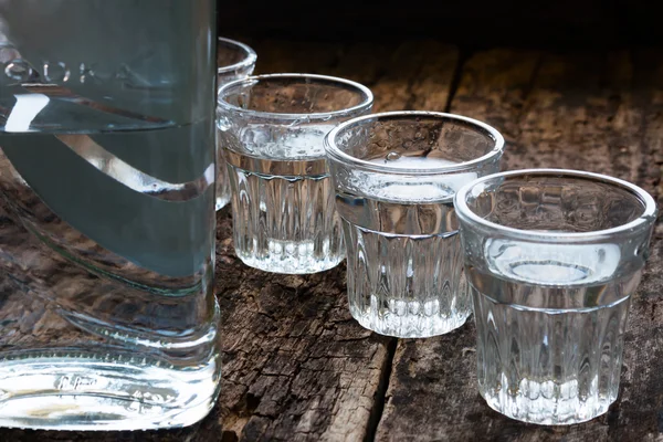 Bottle of vodka and shot glasses on a wooden background close up