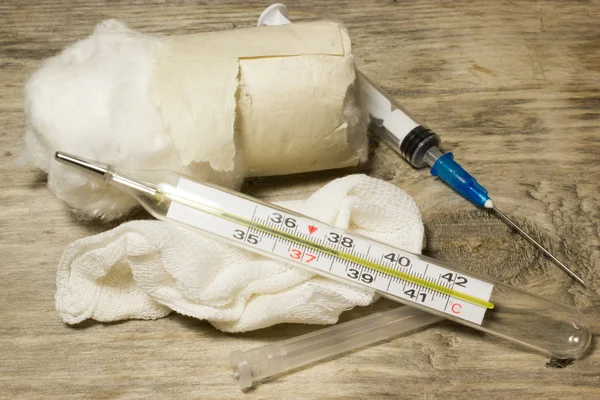 Plastic disposable syringe and thermometer on wooden background.