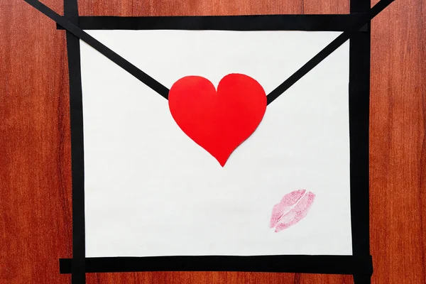 Hand made envelope with heart and lipstick kiss on the wooden ta