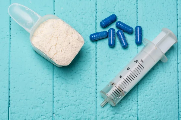Container of milk whey protein, empty injection and pills. Close-up. Blue background